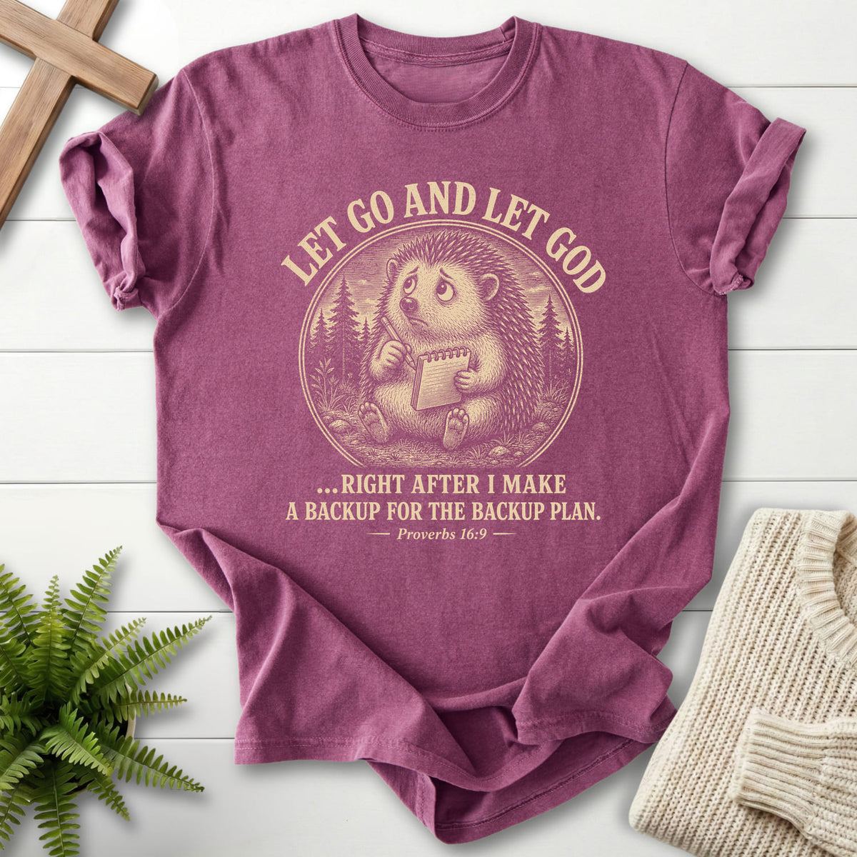Flat lay of a Berry faith-based tee featuring "Let Go and Let God Backup Plan T-Shirt" Proverbs 16:9.