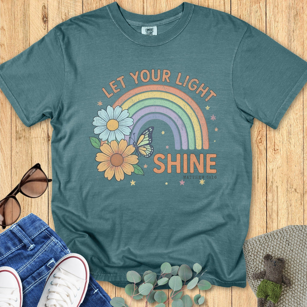 Flatlay of a Comfort Colors 1717 blue spruce “Let Your Light Shine” Matthew 5:16 t-shirt with soft pastel rainbow and floral motif. A charming women’s scripture tee - faith-based apparel for women and modern Christian shirt, sweet Christian mom gift idea that reminds her to shine bright for God.