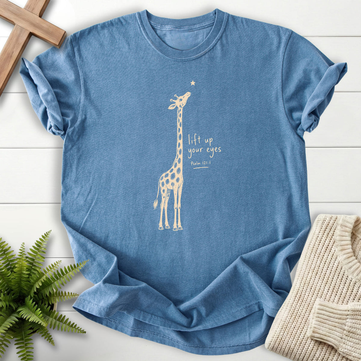 Flat lay of a Blue Jean Christian shirt featuring "Lift Up Your Eyes Giraffe T-Shirt" Psalm 121:1.
