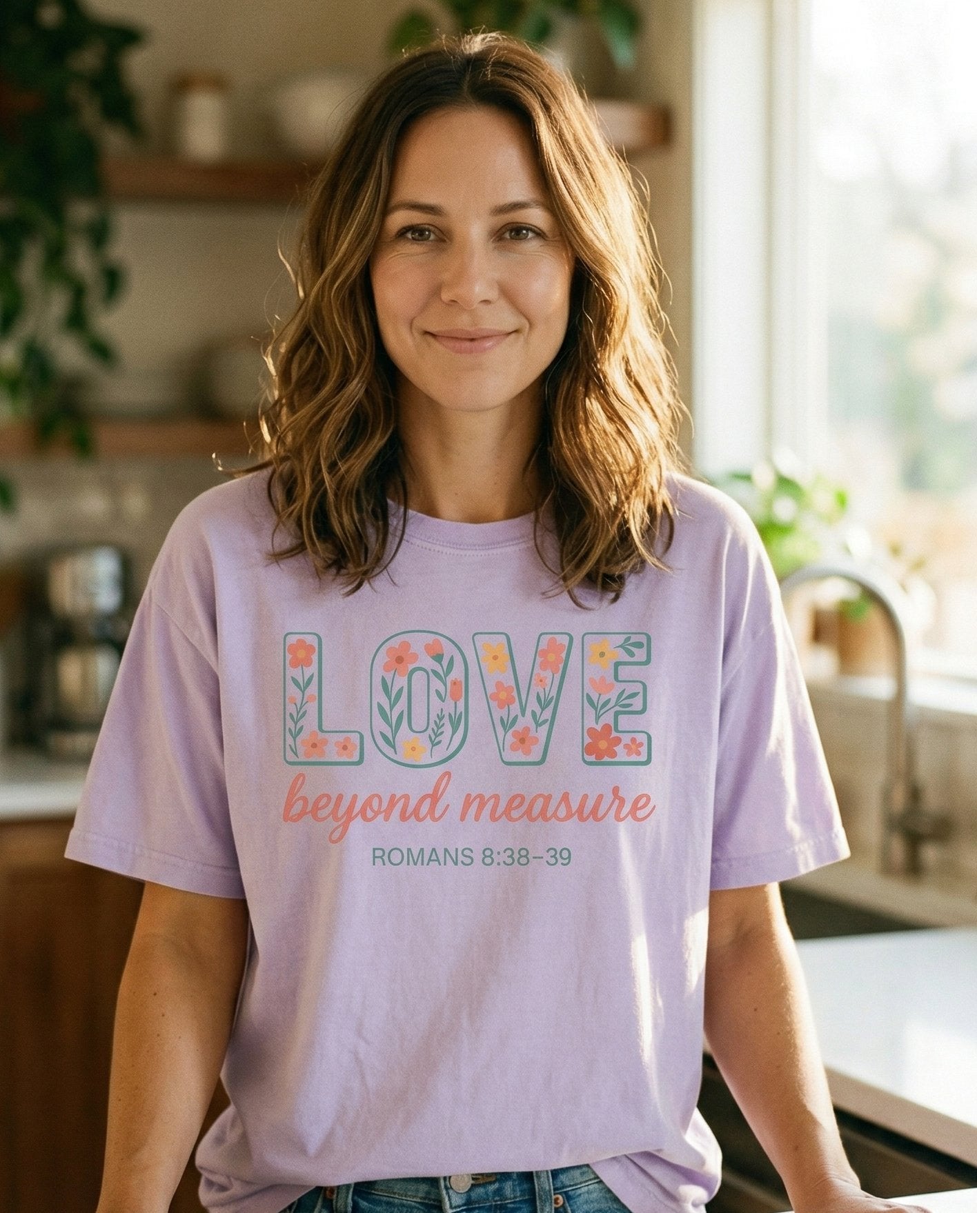 Love Beyond Measure – Orchid women's Christian tee, lifestyle photo in morning kitchen setting – Block letters spelling 'LOVE' filled with colorful floral illustration – Romans 8:38-39 – She Wears Faith