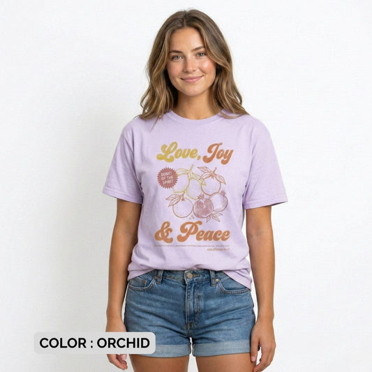 Christian woman wearing an orchid Comfort Colors 1717 “Love, Joy & Peace” tshirt inspired by Galatians 5:22, styled with casual denim shorts. Soft pastel US faith wear featuring fruit illustration and Fruit of the Spirit message, perfect for modern Christian women’s apparel.