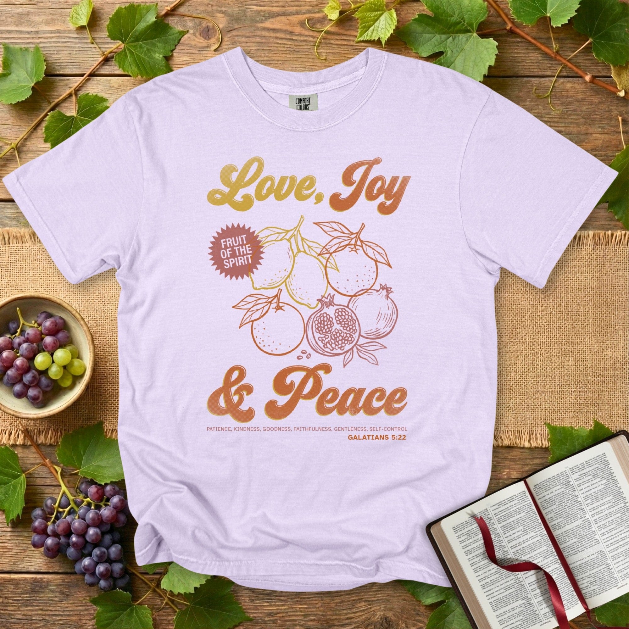 “Comfort Colors 1717 orchid Christian women tee featuring a Fruit of the Spirit design with lemons and pomegranates and the words Love, Joy & Peace from Galatians 5:22. Soft pastel US faith wear with a vintage Christian aesthetic.