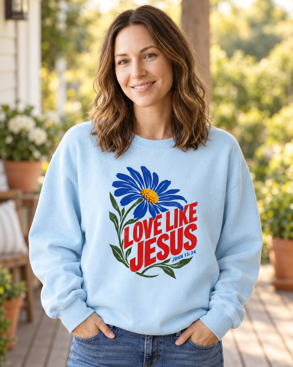 Love Like Jesus Daisy, Chambray women's Christian sweatshirt, lifestyle photo in sunny porch, Blue daisy with bold red LOVE LIKE JESUS lettering, She Wears Faith