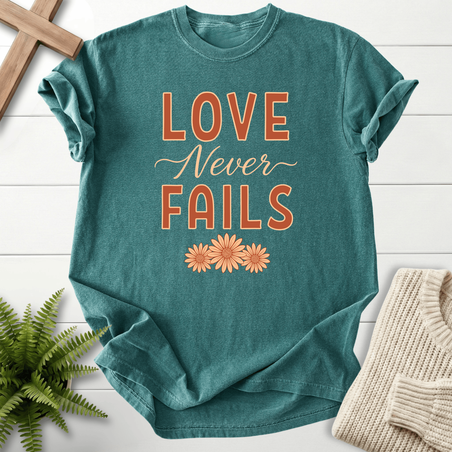Blue Spruce women's Christian t-shirt with bold lettering and daisy trio, inspired by 1 Corinthians 13:8.