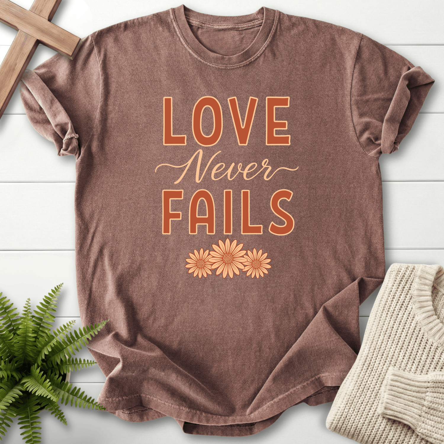 Espresso Scripture shirt with orange block lettering and small floral accent, inspired by 1 Corinthians 13:8.