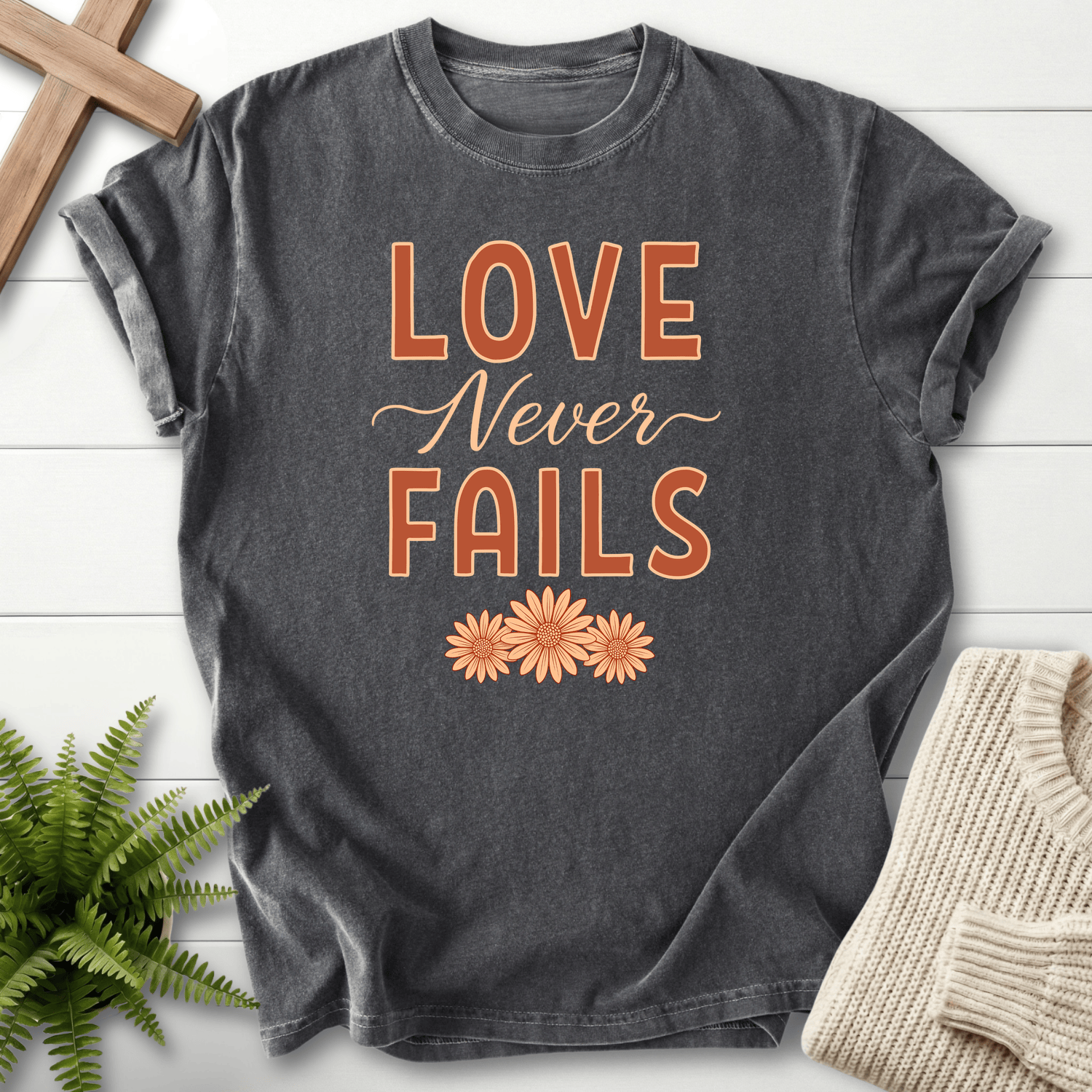 Pepper garment-dyed Christian t-shirt with "Love Never Fails" floral script, inspired by 1 Corinthians 13:8.