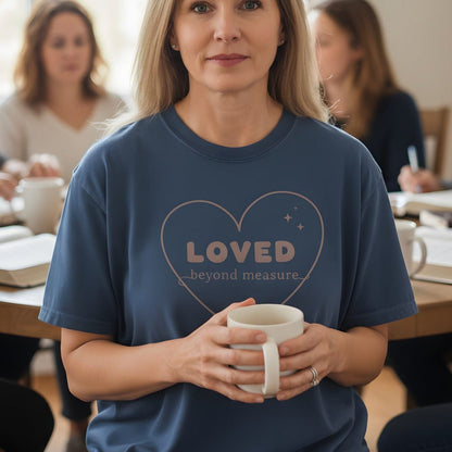 Woman holding a coffee mug in a Bible study group wearing a Comfort Colors 1717 midnight “Loved Beyond Measure – Ephesians 3:18-19” t-shirt. A gentle women’s scripture tee — heartfelt faith-based apparel for women and modern Christian shirt, perfect Christian mom gift idea.