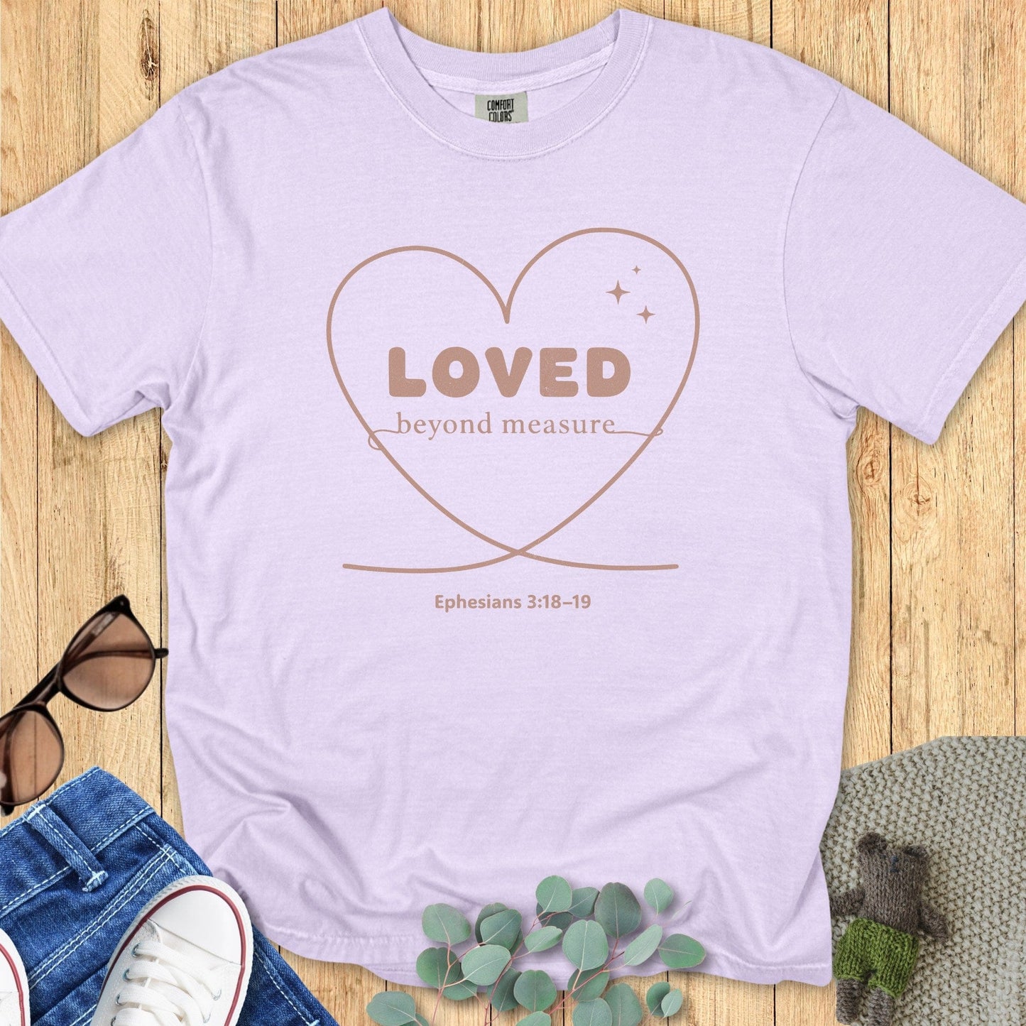 Flatlay of a Comfort Colors 1717 orchid “Loved Beyond Measure – Ephesians 3:18-19” t-shirt with simple heart line art and soft neutral print. A feminine women’s scripture tee — inspiring faith-based apparel for women and modern Christian shirt, thoughtful Christian mom gift idea.
