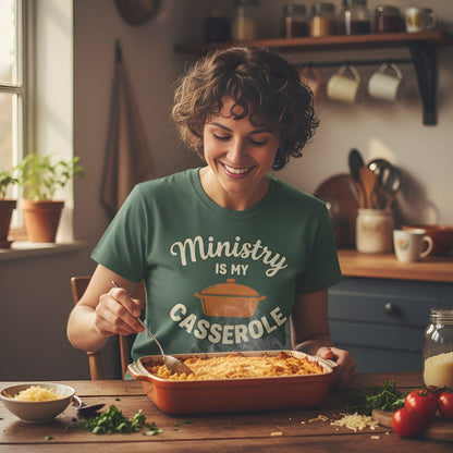 Woman in a kitchen wearing a green t-shirt with 'Ministry is my Casserole' text, serving a dish from a casserole.