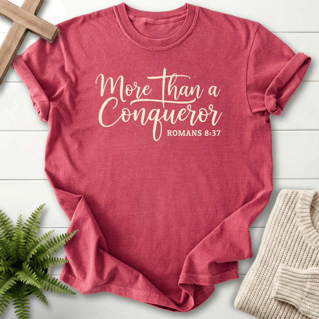 Crimson women's Scripture shirt with 'More Than a Conqueror' flowing cursive lettering, inspired by Romans 8:37.