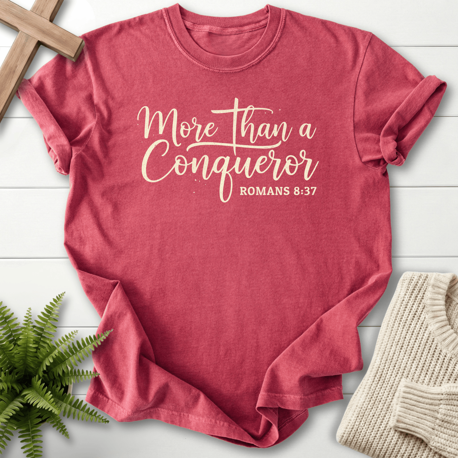 Crimson women's Scripture shirt with 'More Than a Conqueror' flowing cursive lettering, inspired by Romans 8:37.