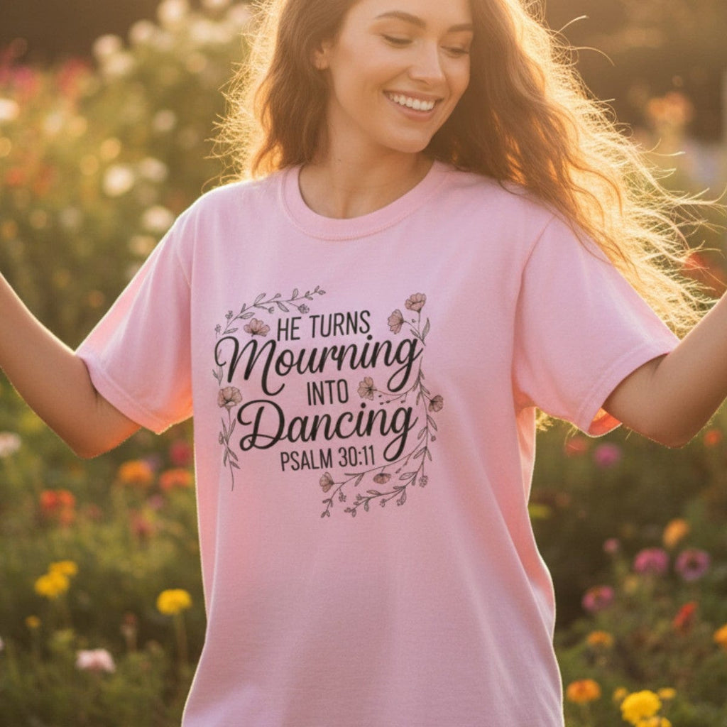 Smiling woman dancing in a garden at sunset wearing a Comfort Colors 1717 blossom “He Turns Mourning Into Dancing – Psalm 30:11” t-shirt. A radiant and joyful women’s scripture tee — perfect modern Christian shirt and heartfelt Christian mom gift idea.