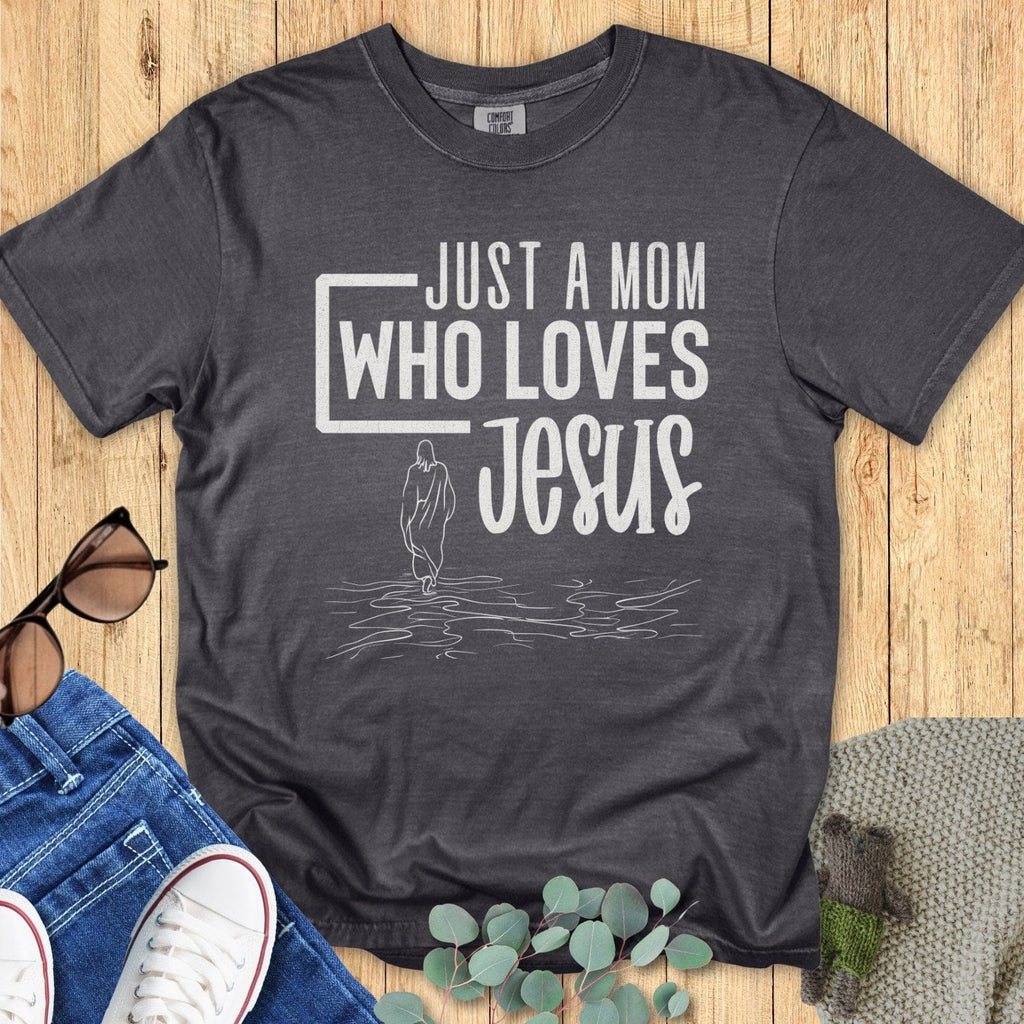 Flatlay of a Comfort Colors 1717 pepper “Just a Mom Who Loves Jesus” t-shirt featuring minimalist Jesus walking on water design. A stylish women’s scripture tee — faith-based apparel for women and modern Christian shirt, meaningful Christian mom gift idea.