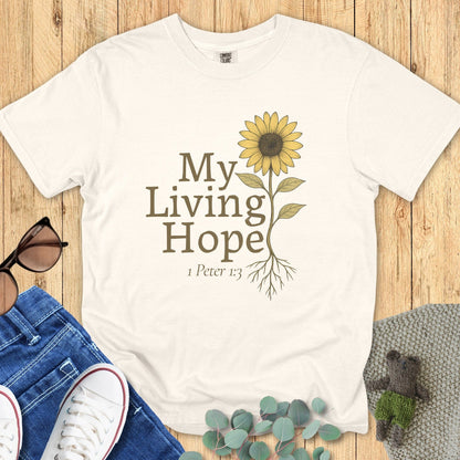 Flatlay of a Comfort Colors 1717 ivory “My Living Hope – 1 Peter 1:3” t-shirt with hand-drawn sunflower and rooted design. A beautiful women’s scripture tee — faith-based apparel for women and modern Christian shirt, perfect Christian mom gift idea.