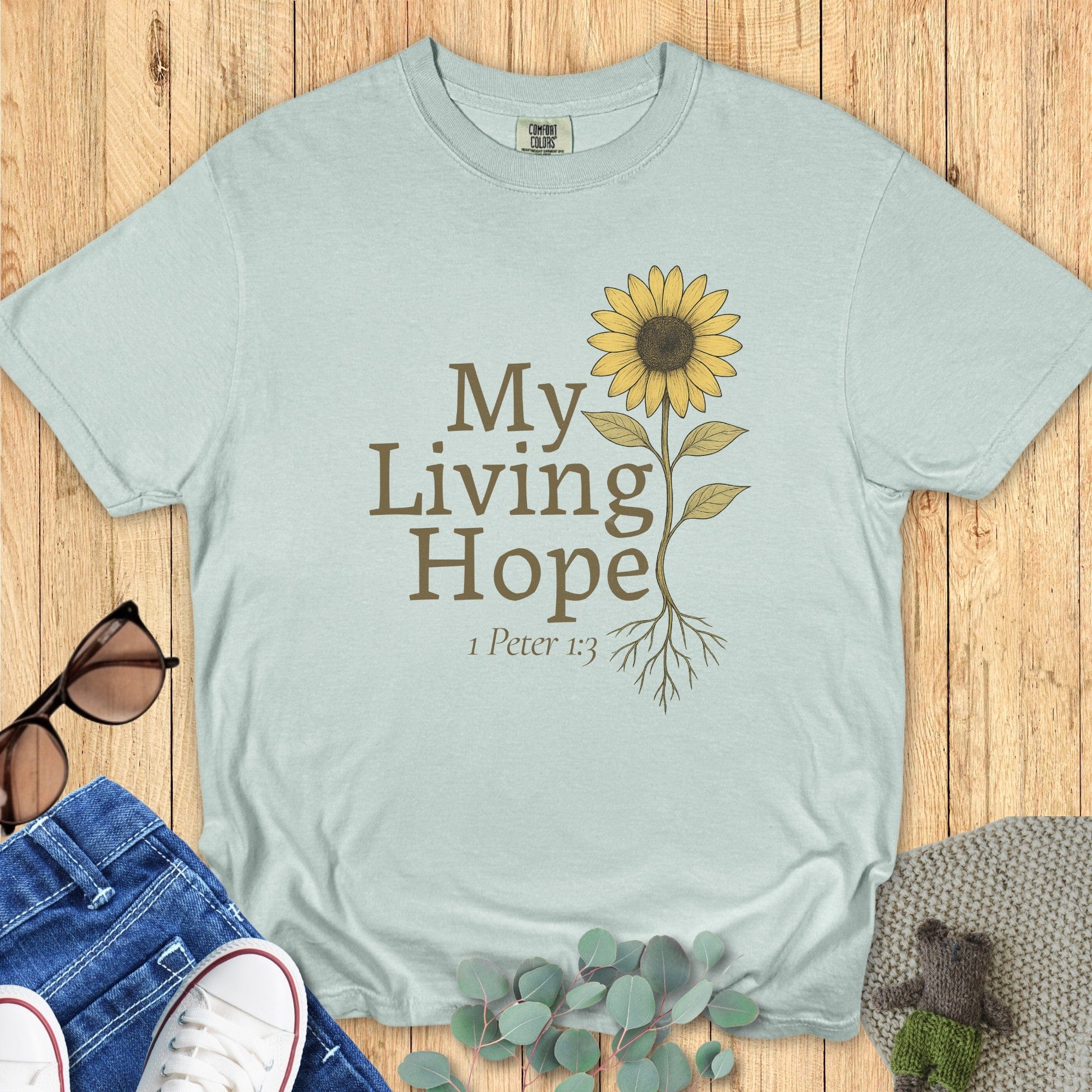 Flatlay of a Comfort Colors 1717 bay “My Living Hope – 1 Peter 1:3” t-shirt featuring a delicate sunflower graphic. A graceful women’s scripture tee — inspiring faith-based apparel for women and modern Christian shirt, lovely Christian mom gift idea.