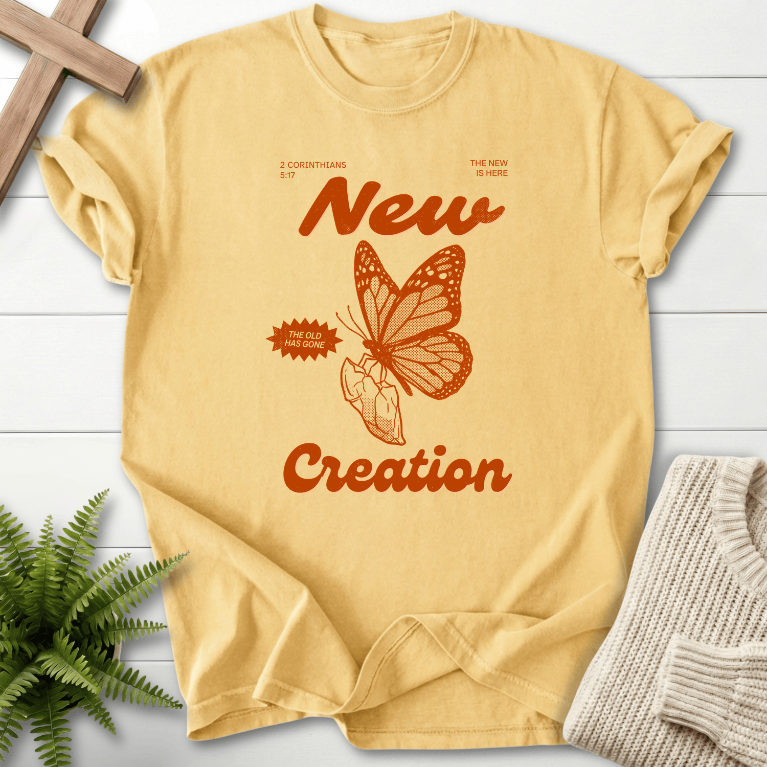 Butter yellow women's Bible verse tee with monarch butterfly and 'New Creation' retro orange text, inspired by 2 Corinthians 5:17.
