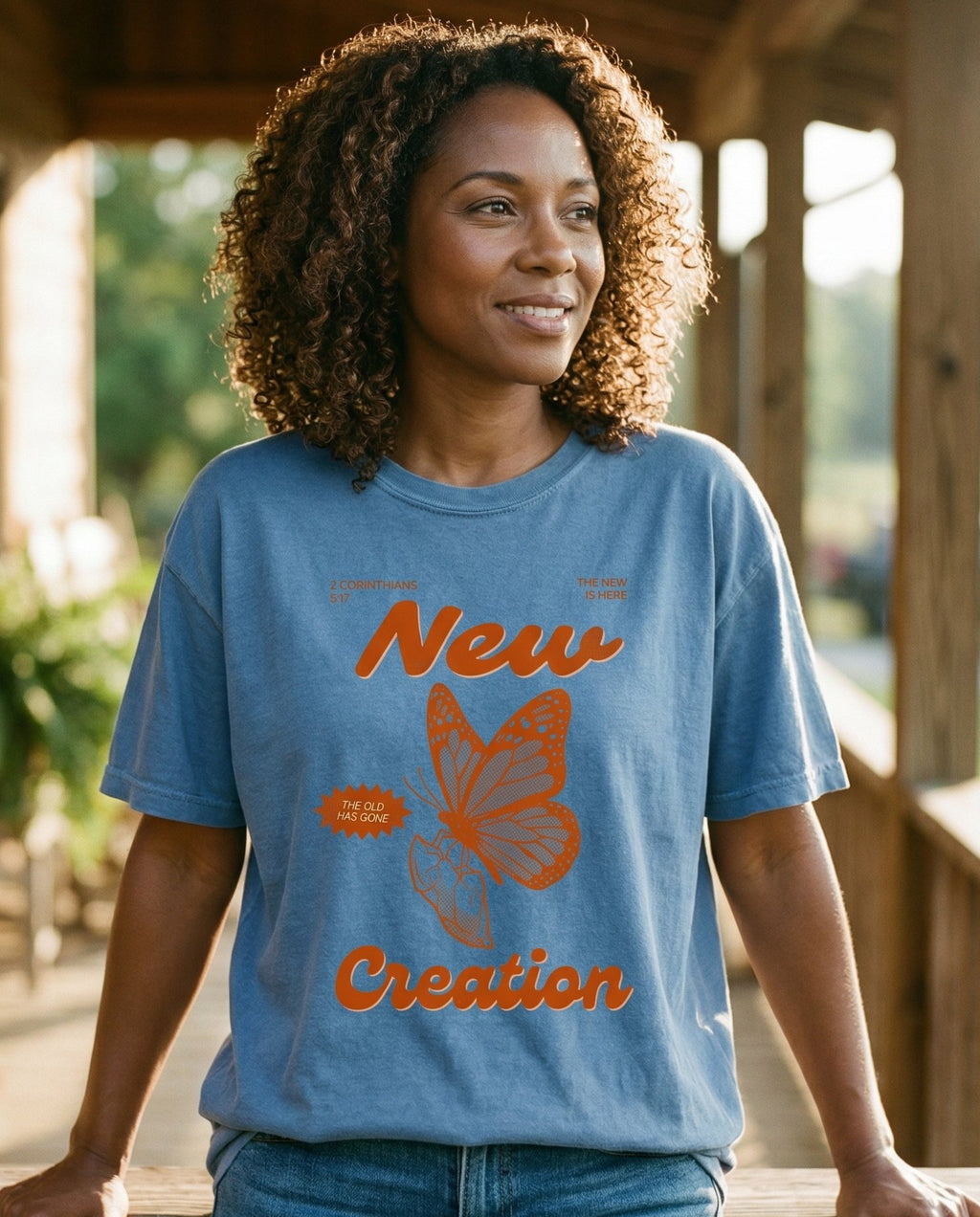 New Creation Butterfly – Blue Jean women's Christian tee, lifestyle photo in sunny porch – Retro poster-style design with a monarch butterfly illustration and bo – 2 Corinthians 5:17 – She Wears Faith