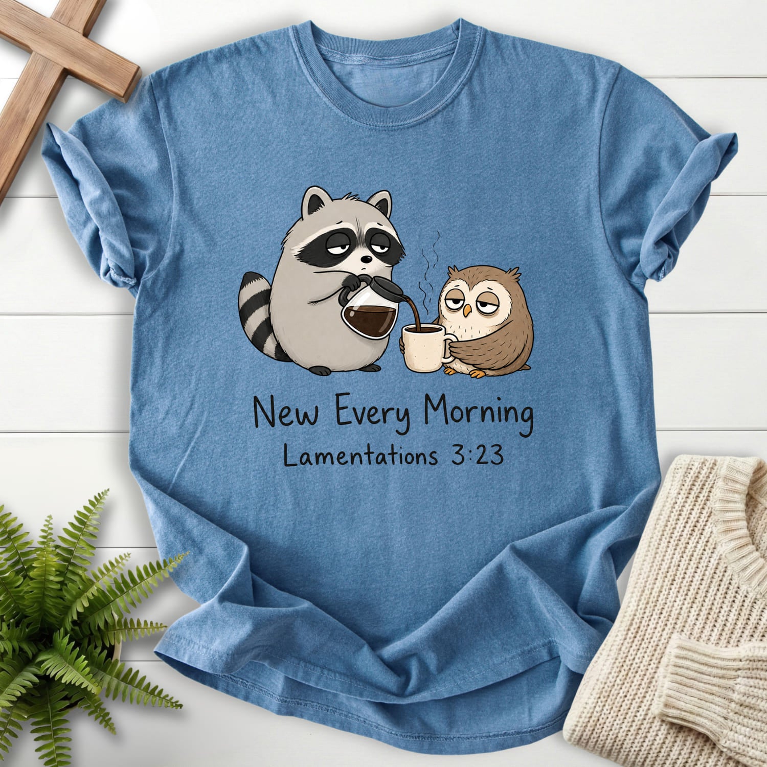 Flatlay of a Blue Jean faith-based tee with "New Every Morning Raccoon Owl T-Shirt" Lamentations 3:23.