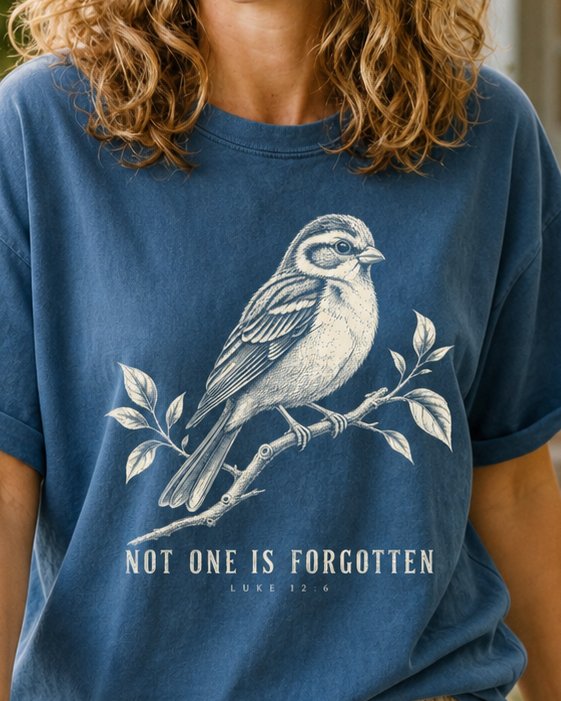 Not One Is Forgotten Luke 12 6 - Midnight women's Christian tee, lifestyle photo in cottage doorway - Engraved sparrow perched on a leafy branch - Luke 12:6 - She Wears Faith