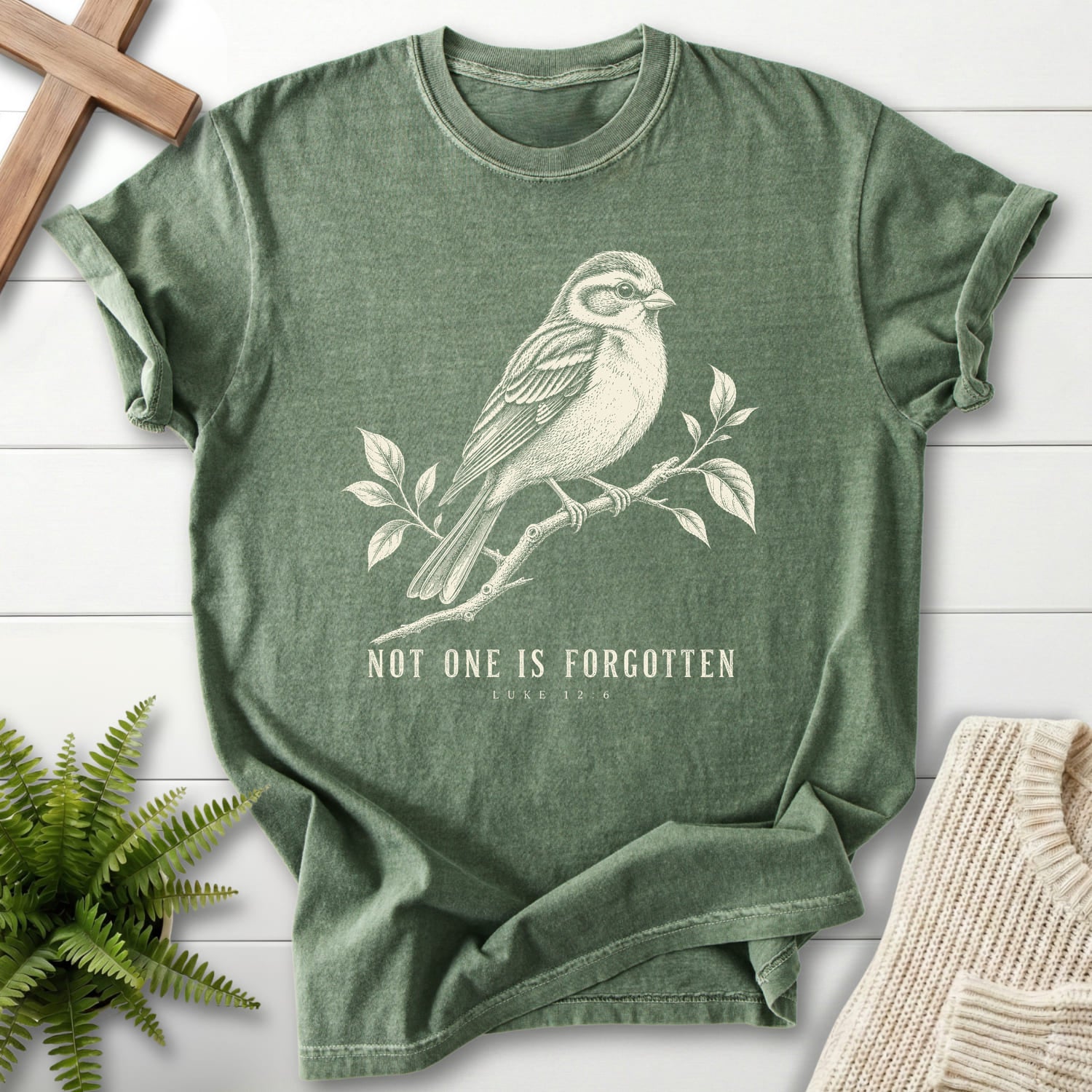 Flatlay of a Moss Comfort Colors 1717 garment-dyed Christian tee with "Not One Is Forgotten Luke 12:6 T-Shirt" design.