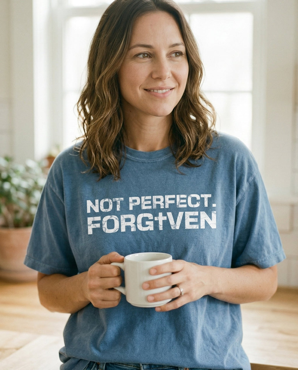 Not Perfect. Forgiven – Blue Jean women's Christian tee, lifestyle photo in morning kitchen setting – Distressed grunge block lettering reading 'Not Perfect – She Wears Faith