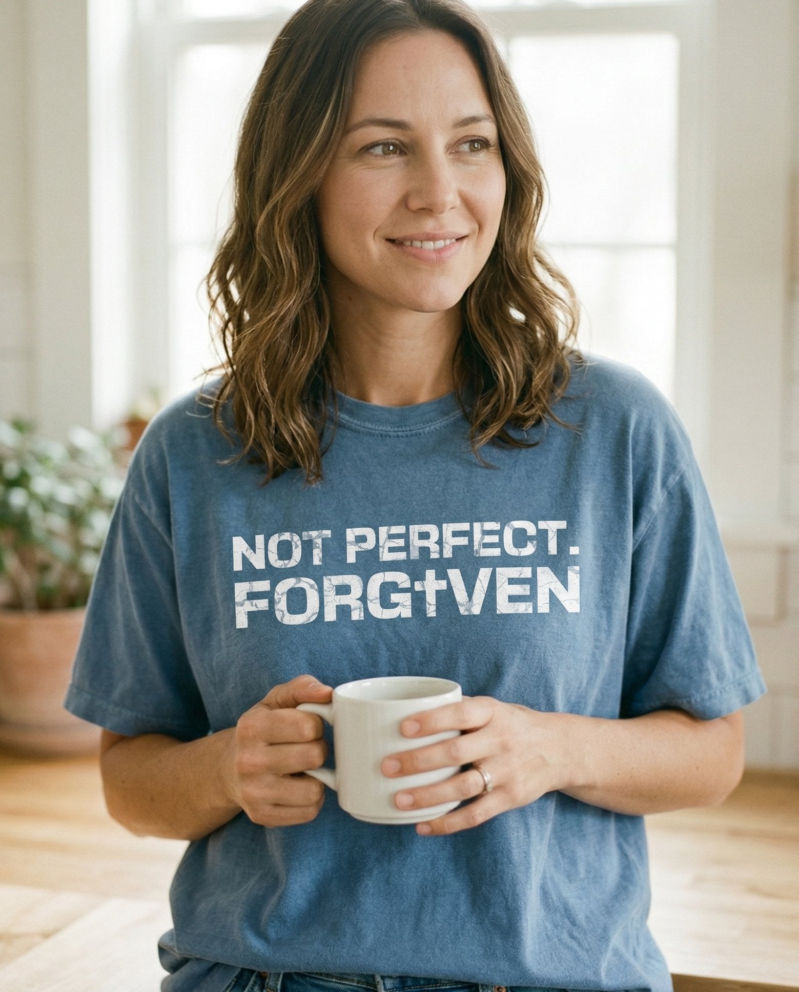 Not Perfect. Forgiven – Blue Jean women's Christian tee, lifestyle photo in morning kitchen setting – Distressed grunge block lettering reading 'Not Perfect – She Wears Faith