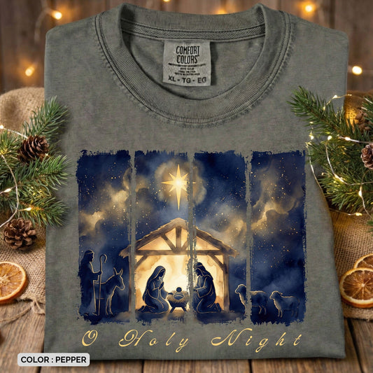 Folded Comfort Colors 1717 pepper Christian women tee showcasing a watercolor “O Holy Night” nativity illustration with Mary, Joseph, baby Jesus, shepherds, and night sky. Cozy and elegant US faith wear photographed with Christmas greenery and warm lights.