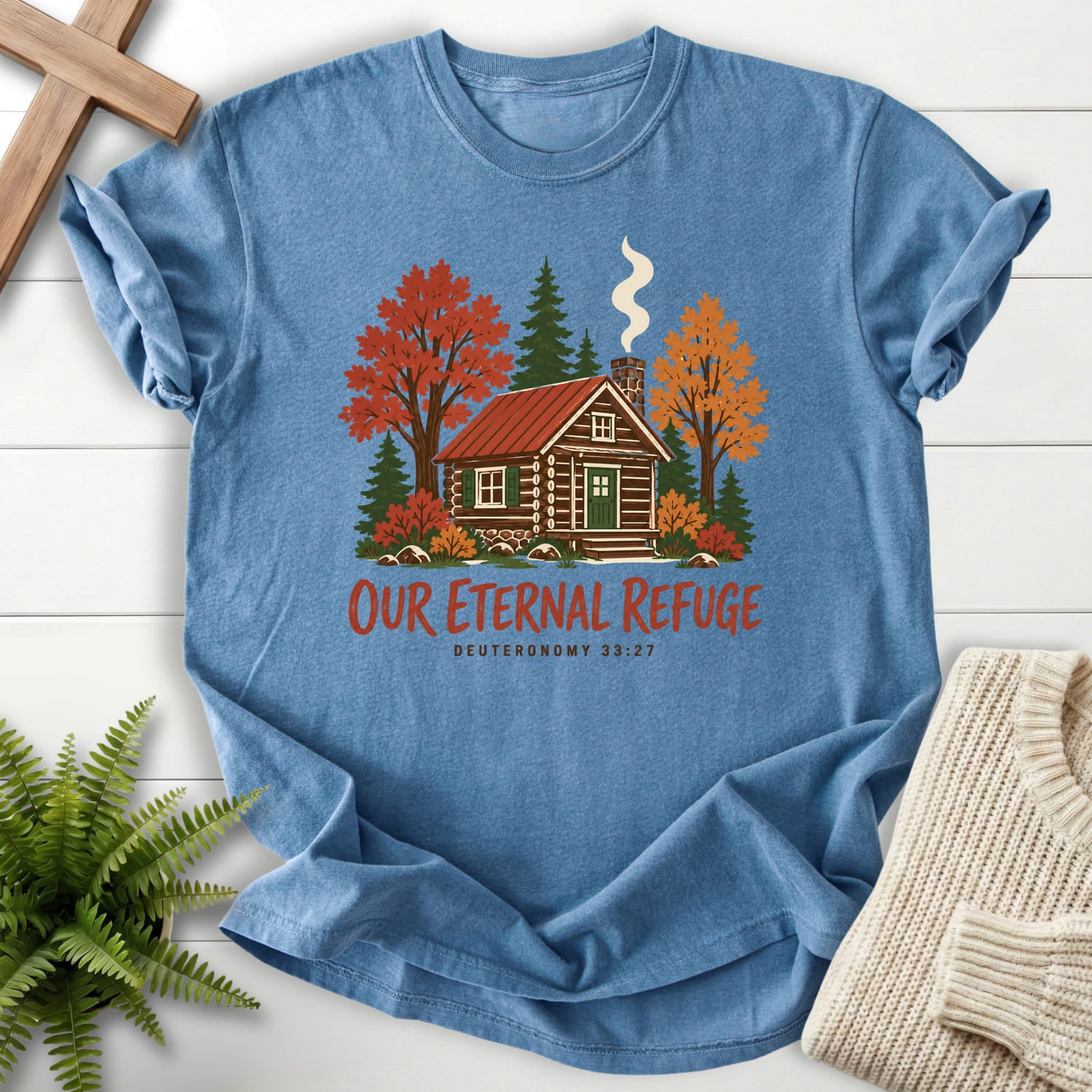 Flat lay of a Blue Jean Christian graphic tee featuring "Our Eternal Refuge Autumn Faith T-Shirt" Deuteronomy 33:27.