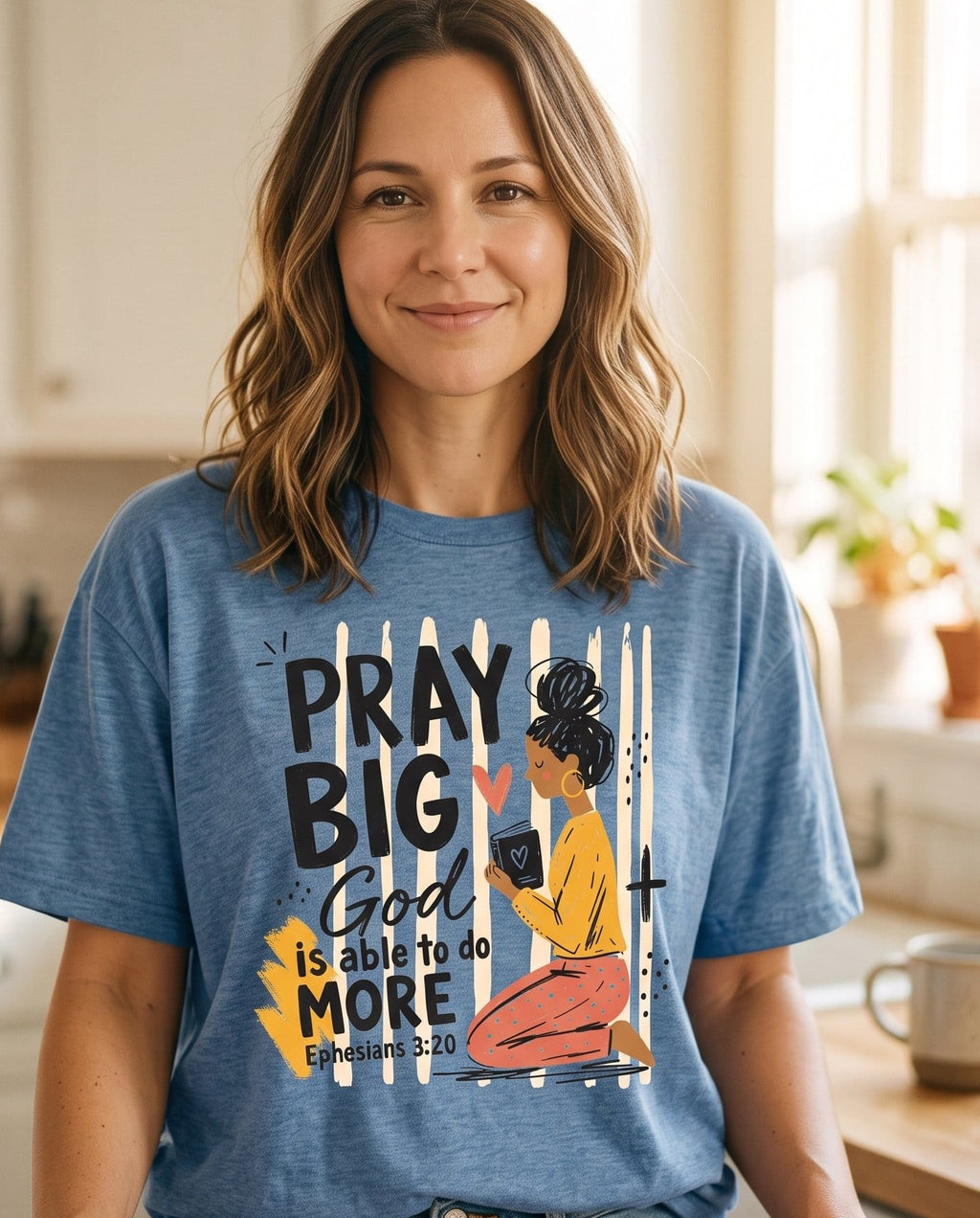 Pray Big God Is Able – Blue Jean women's Christian tee, lifestyle photo in morning kitchen setting – Illustrated woman kneeling in prayer with a Bible – Ephesians 3:20 – She Wears Faith