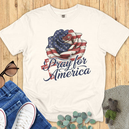 Flatlay of a Comfort Colors 1717 ivory “Pray for America” t-shirt featuring a distressed American flag rose design. A classic women’s scripture tee — faith-based apparel for women and modern Christian shirt, ideal Christian mom gift idea for prayer warriors and believers.