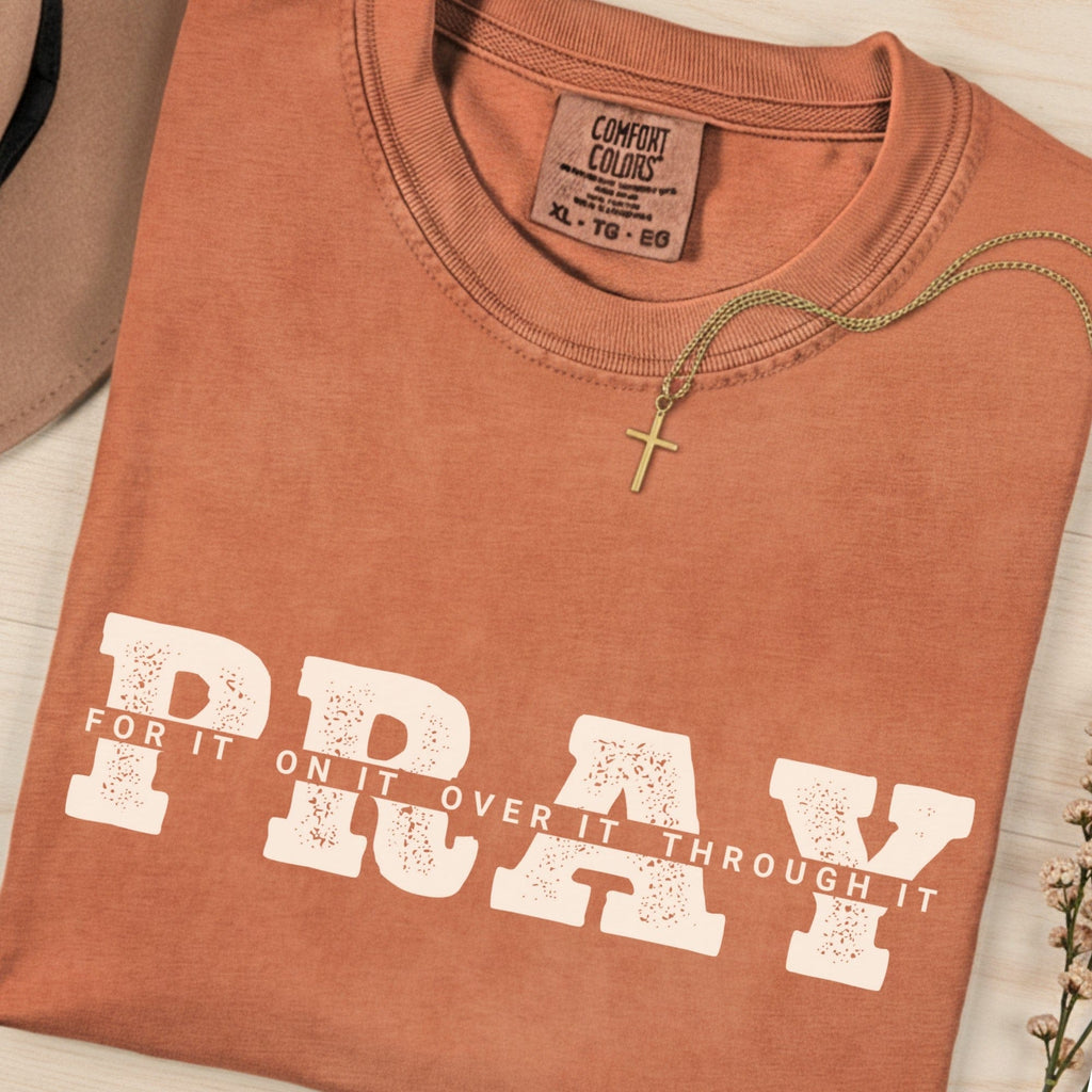 Folded Comfort Colors 1717 yam “PRAY for it, on it, over it, through it” t-shirt featuring bold collegiate lettering and cross necklace. A warm women’s scripture tee -  faith-based apparel for women and modern Christian shirt, thoughtful Christian mom gift idea.
