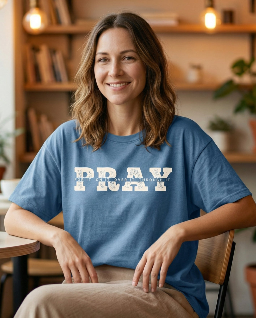 Pray for It – Blue Jean women's Christian tee, lifestyle photo in cozy café – Bold varsity block letters spelling 'PRAY' with smaller text inside ea – She Wears Faith