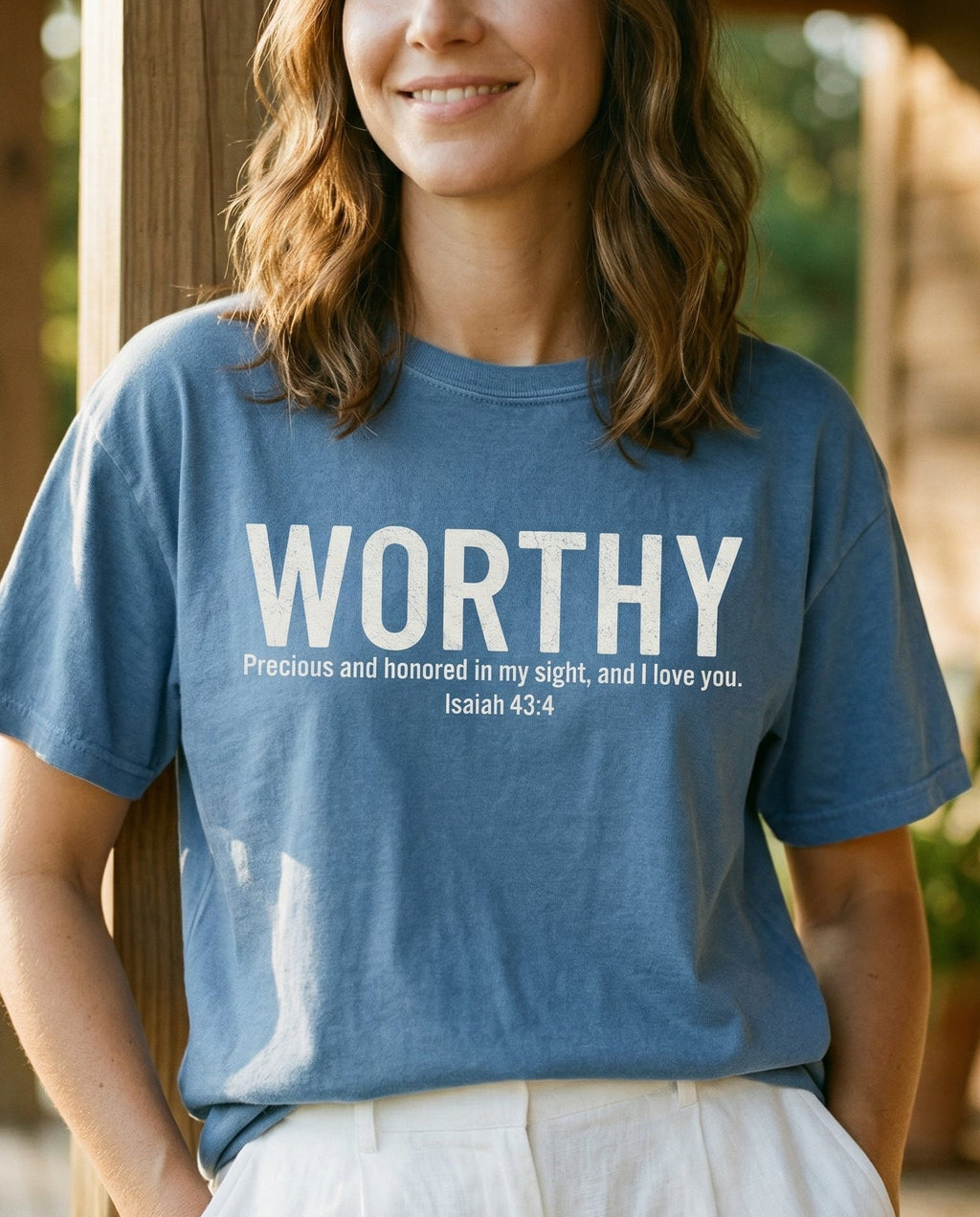 Precious and honored – Blue Jean women's Christian tee, lifestyle photo in sunny porch – Bold grunge-style text reading WORTHY with subtitle 'Precious and hono – Isaiah 43:4 – She Wears Faith