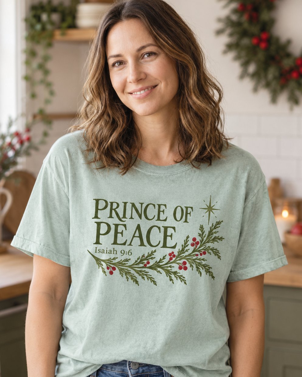 Prince of Peace, Bay women's Christian tee, lifestyle photo in cozy holiday setting, Prince of Peace lettering with an evergreen branch and red berries, Isaiah 9:6, She Wears Faith.