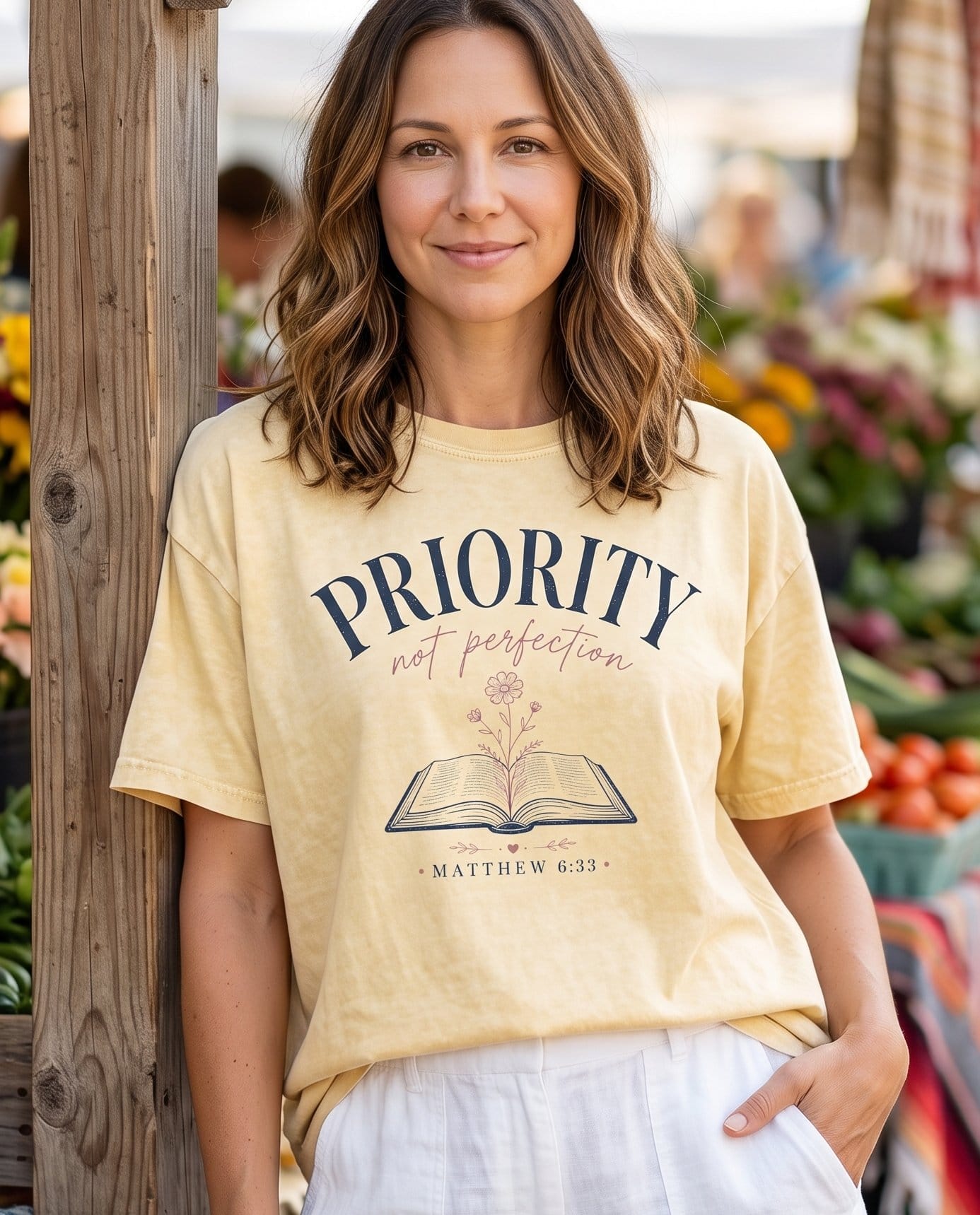 Priority Not Perfection Matthew 6:33 – Banana women's Christian tee, lifestyle photo in farmers market – Deep navy arched serif 'PRIORITY' with soft pink script 'not perfectio – Matthew 6:33 – She Wears Faith