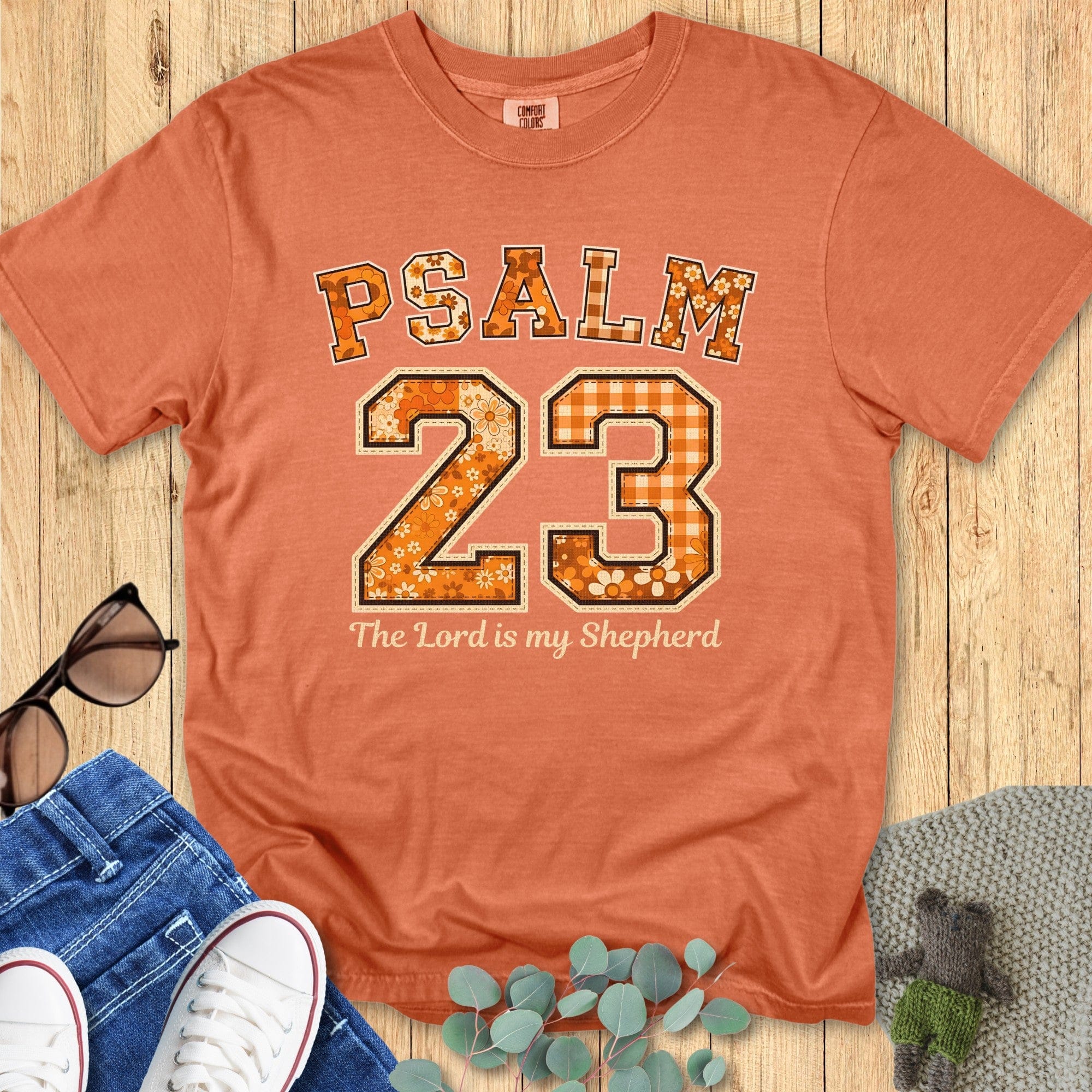 Flatlay of a Comfort Colors 1717 yam “Psalm 23 — The Lord is my Shepherd” t-shirt with vintage orange and cream patchwork numbers. A stylish women’s scripture tee -  faith-based apparel for women and modern Christian shirt, perfect Christian mom gift idea for autumn.