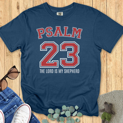 Flatlay of a Comfort Colors 1717 midnight blue “Psalm 23 The Lord is My Shepherd” t-shirt with bold varsity lettering. A stylish women’s scripture tee — faith-based apparel for women and modern Christian shirt, perfect Christian mom gift idea.