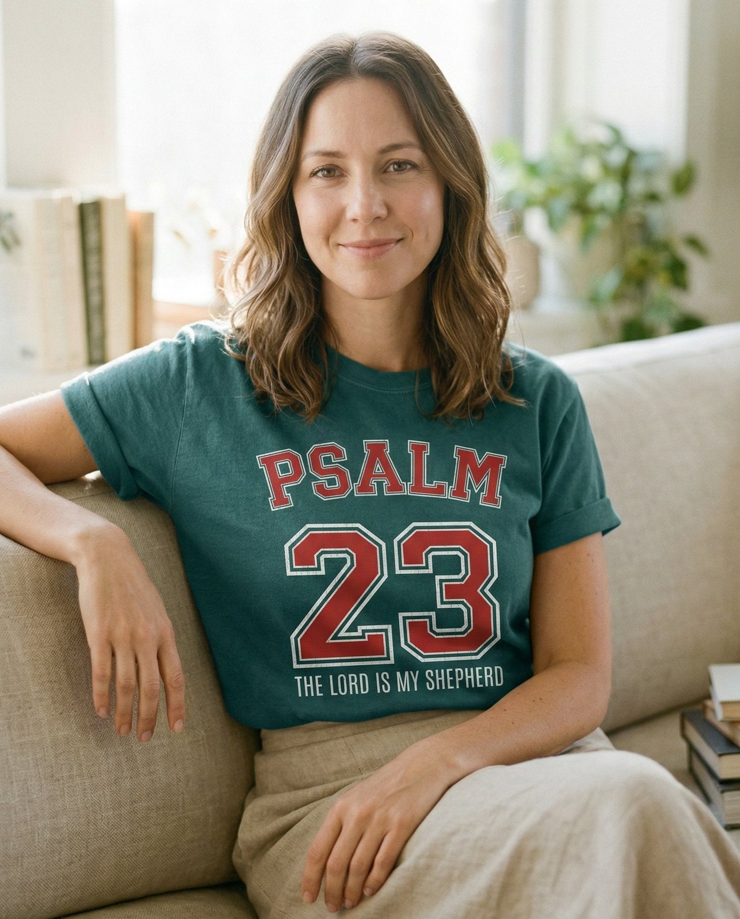 Psalm 23 – Blue Spruce women's Christian tee, lifestyle photo in cozy living room – Bold varsity-style PSALM 23 in red with white outline and block text ' – Psalm 23 – She Wears Faith
