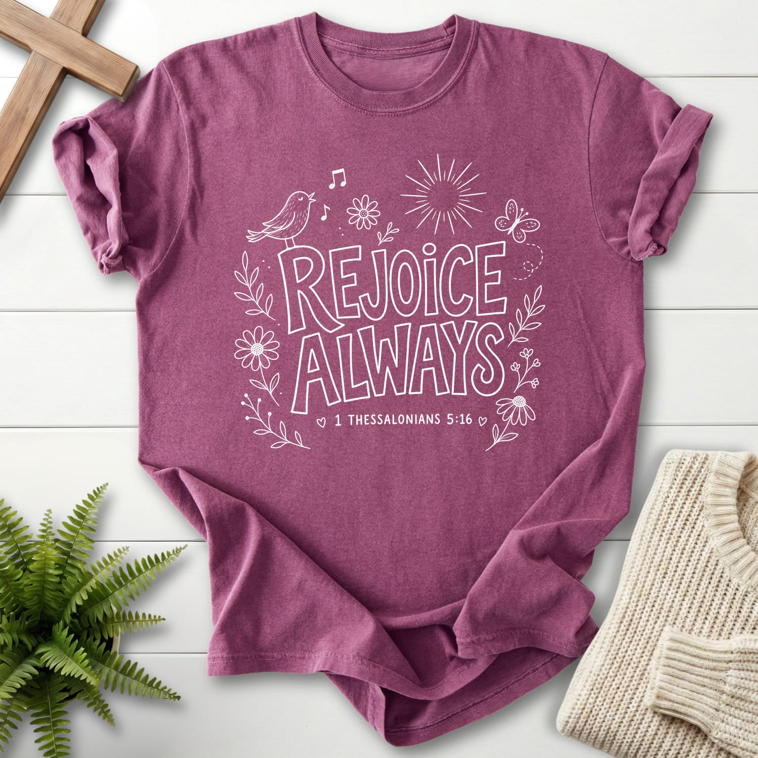 Flat lay of a Berry Christian t-shirt for women featuring butterfly artwork with "Rejoice Always T-Shirt" 1 Thessalonians 5:16.