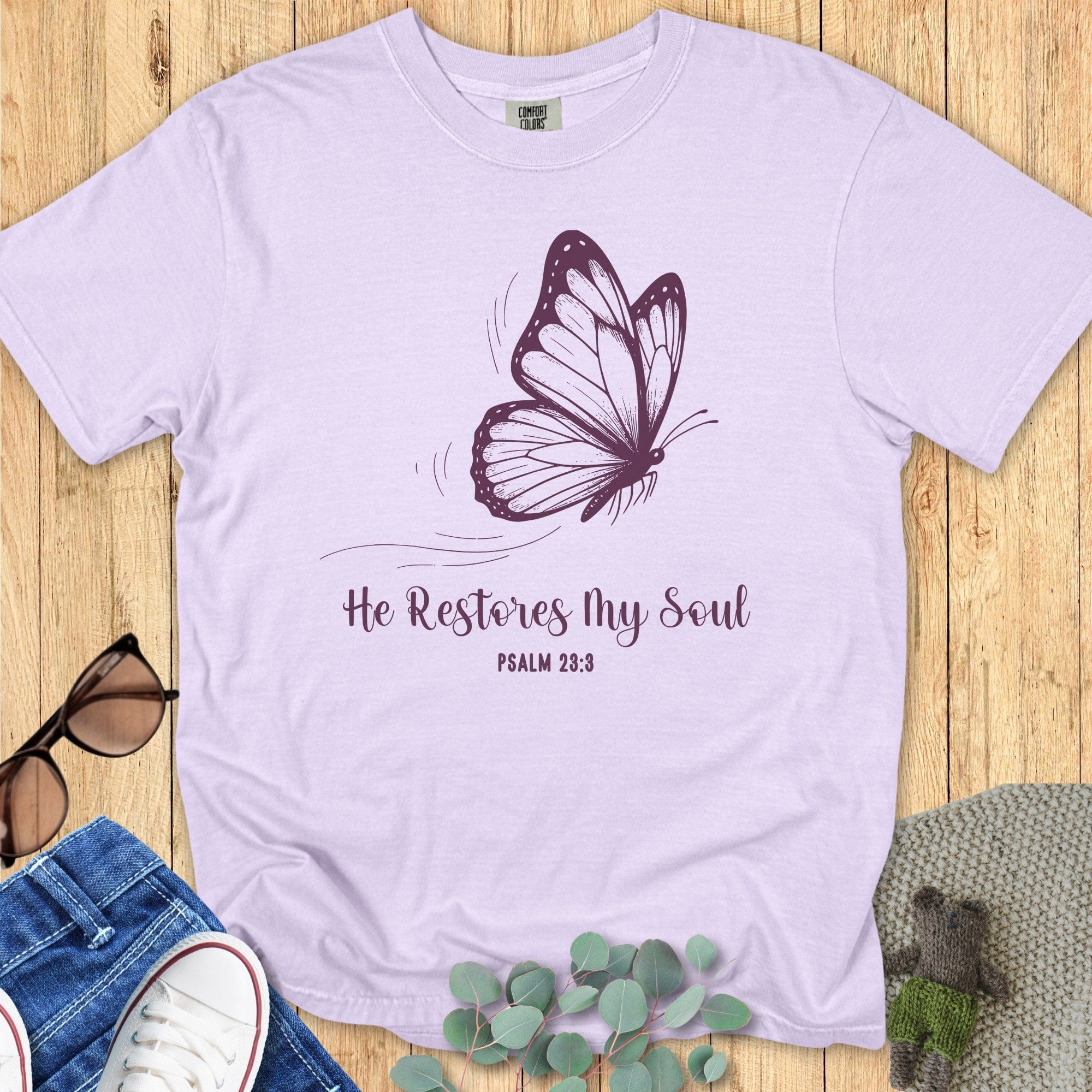 Comfort Colors 1717 orchid “He Restores My Soul – Psalm 23:3” t-shirt with delicate purple butterfly illustration and script lettering. A feminine women’s scripture tee — beautiful faith-based apparel for women and lovely modern Christian shirt, ideal for Christian mom gift ideas.