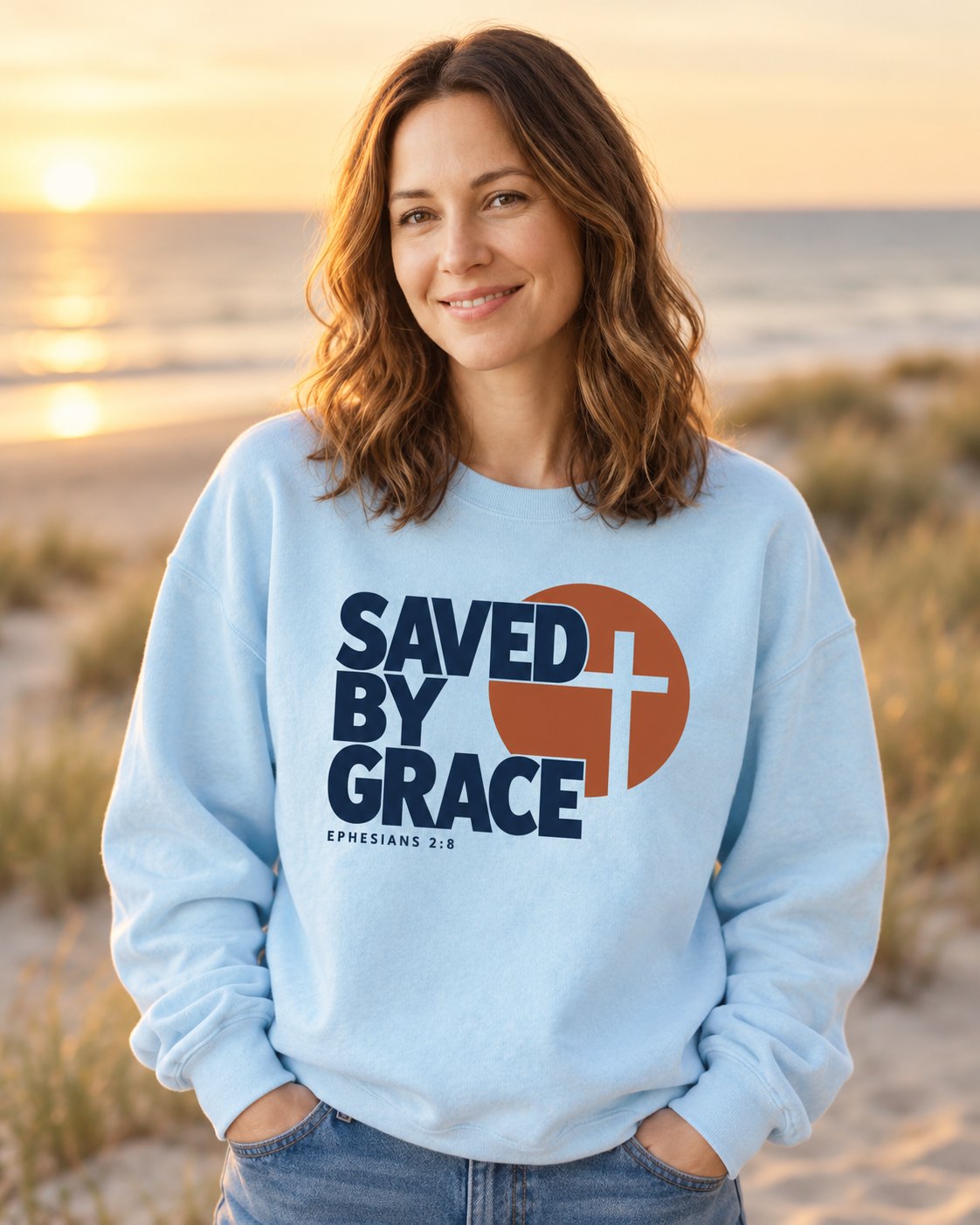 Saved by Grace Bold Cross, Chambray women's Christian sweatshirt, lifestyle photo in seaside setting, Bold SAVED BY GRACE lettering with a cross in a circle, She Wears Faith