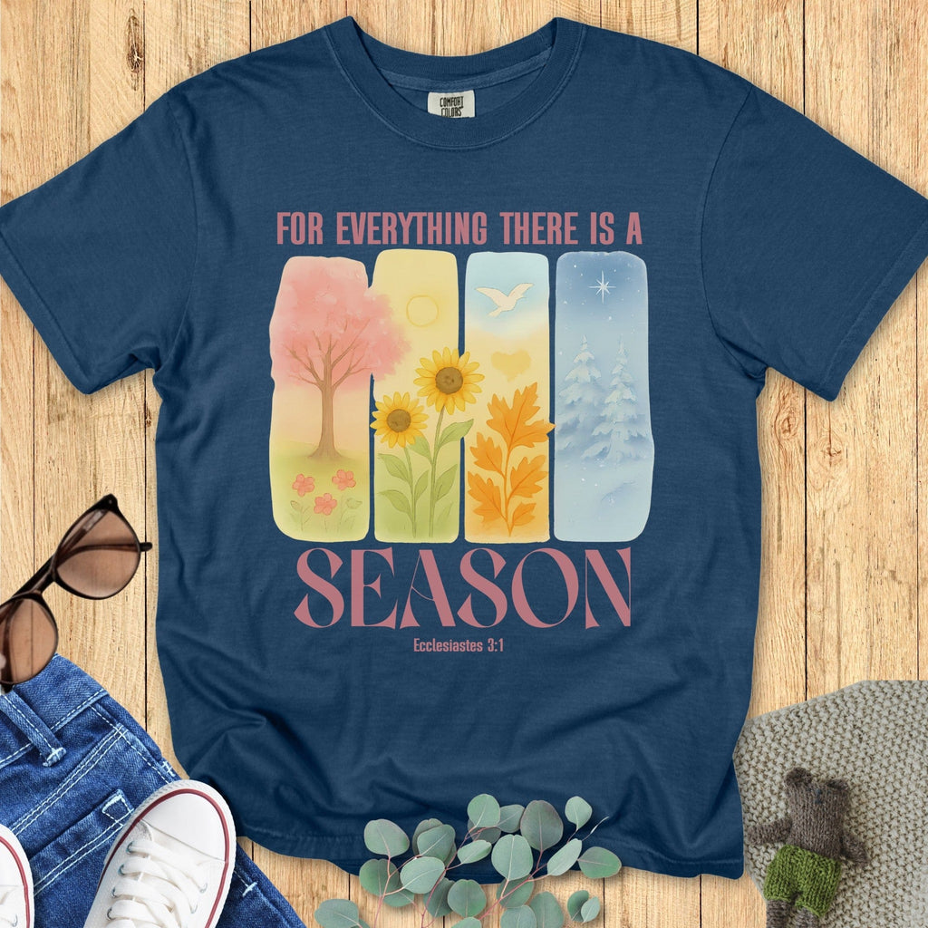 Flatlay of a Comfort Colors 1717 midnight “For Everything There Is a Season – Ecclesiastes 3:1” t-shirt featuring pastel illustrations of all four seasons. A colorful and uplifting women’s scripture tee and faith-based apparel for women.