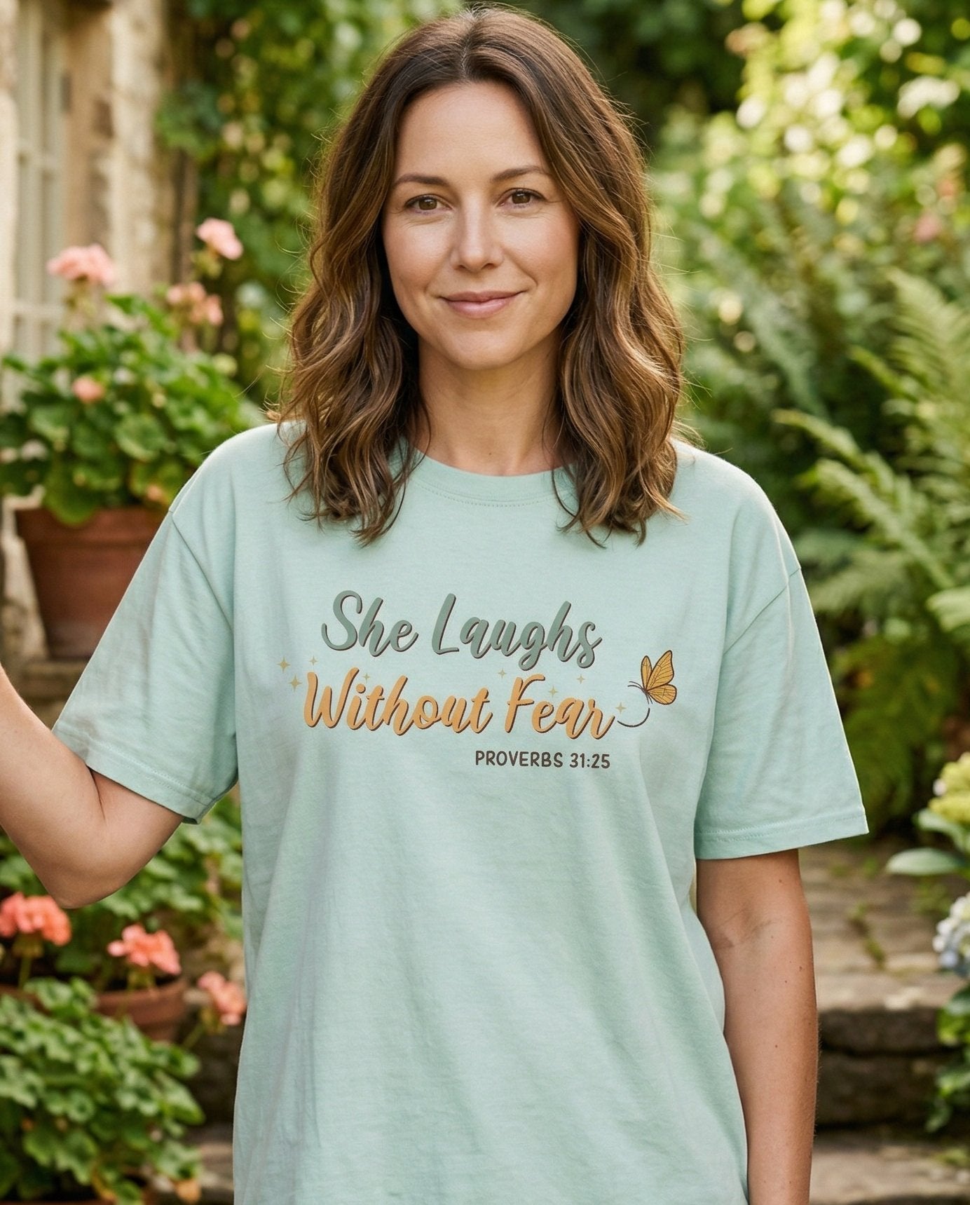 She Laughs Without Fear – Bay women's Christian tee, lifestyle photo in cottage doorway – Colorful script 'She Laughs Without Fear' in teal and gold with a butt – Proverbs 31:25 – She Wears Faith