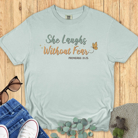 Flatlay of a Comfort Colors 1717 bay “She Laughs Without Fear – Proverbs 31:25” t-shirt featuring soft script typography and a butterfly accent. A stylish women’s scripture tee — faith-based apparel for women and a thoughtful Christian mom gift idea.