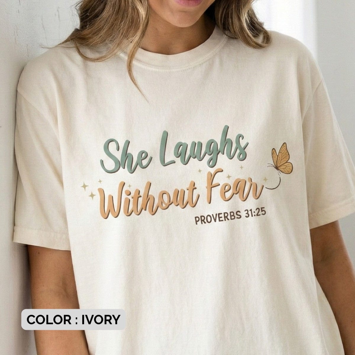Ivory Christian Women's T-Shirt featuring the inspirational phrase "She Laughs Without Fear" in retro-style typography with a butterfly graphic and "Proverbs 31:25" scripture reference.