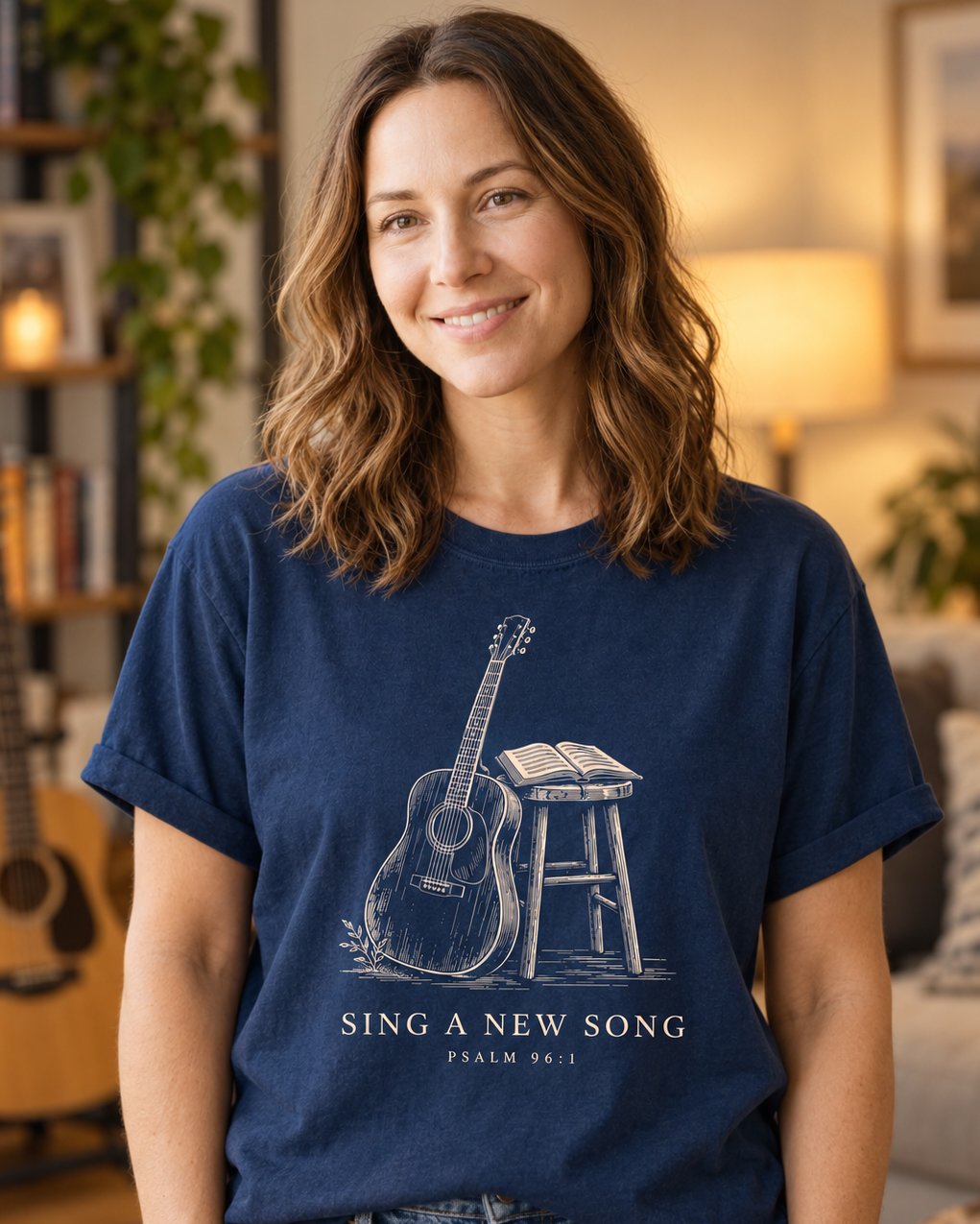 Sing a New Song Guitar, Navy women's Christian tee, lifestyle photo in cozy living room, Line-art acoustic guitar beside a stool with an open songbook, Psalm 96:1, She Wears Faith.