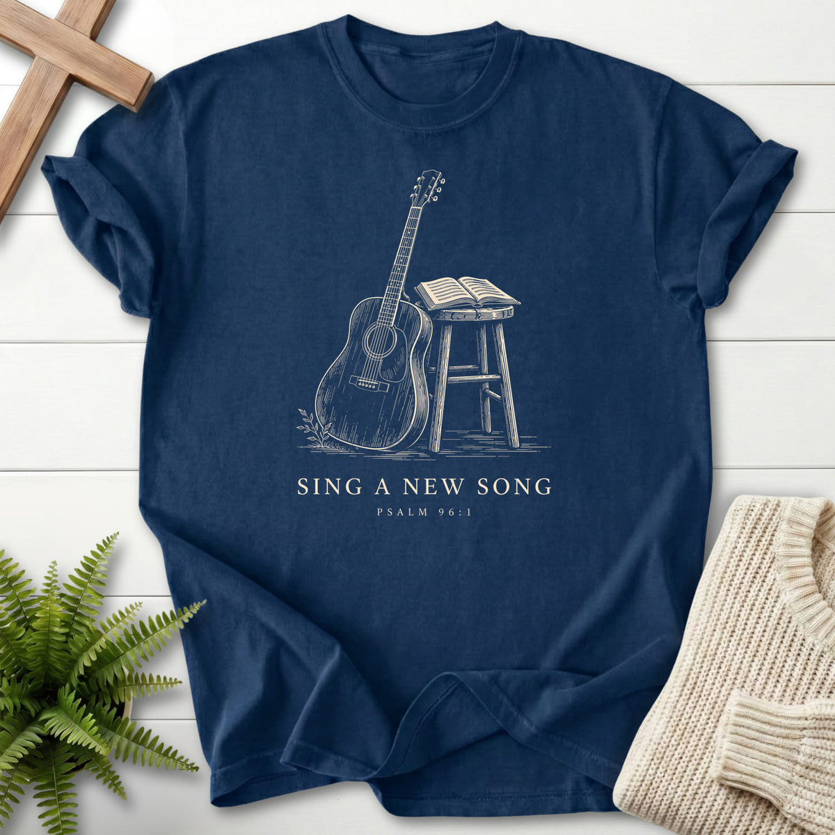 Flatlay of a Navy women's Christian tee with "Sing a New Song Guitar T-Shirt" This Psalm 96:1.