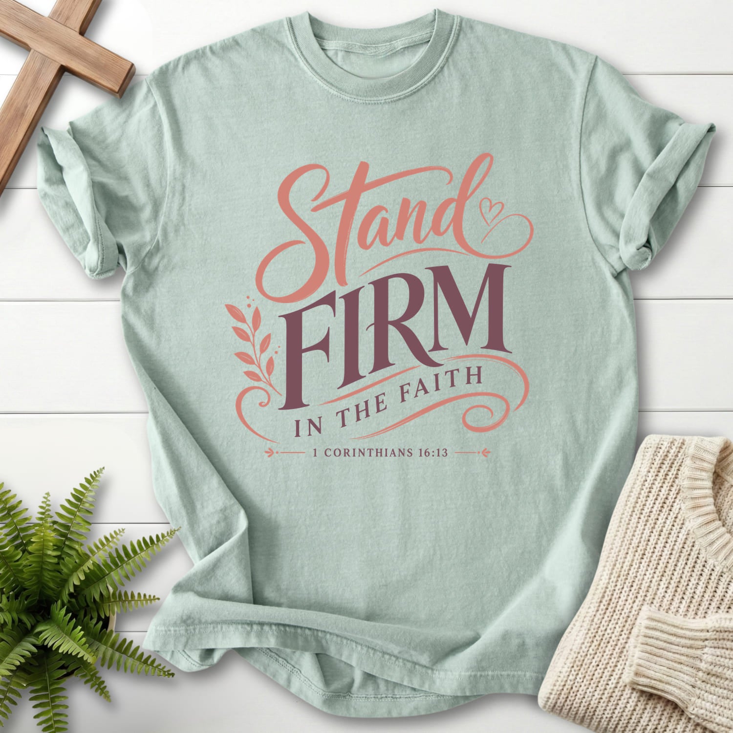 Flat lay of a Bay Scripture shirt featuring script typography with "Stand Firm in the Faith T-Shirt" 1 Corinthians 16:13.