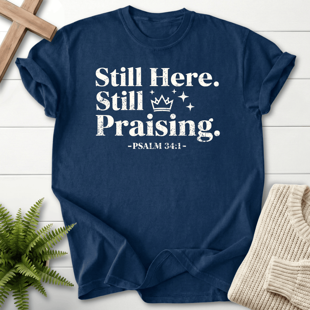 Navy Christian t-shirt for women with distressed white Still Here, Still Praising text, a crown motif, and Psalm 34:1.