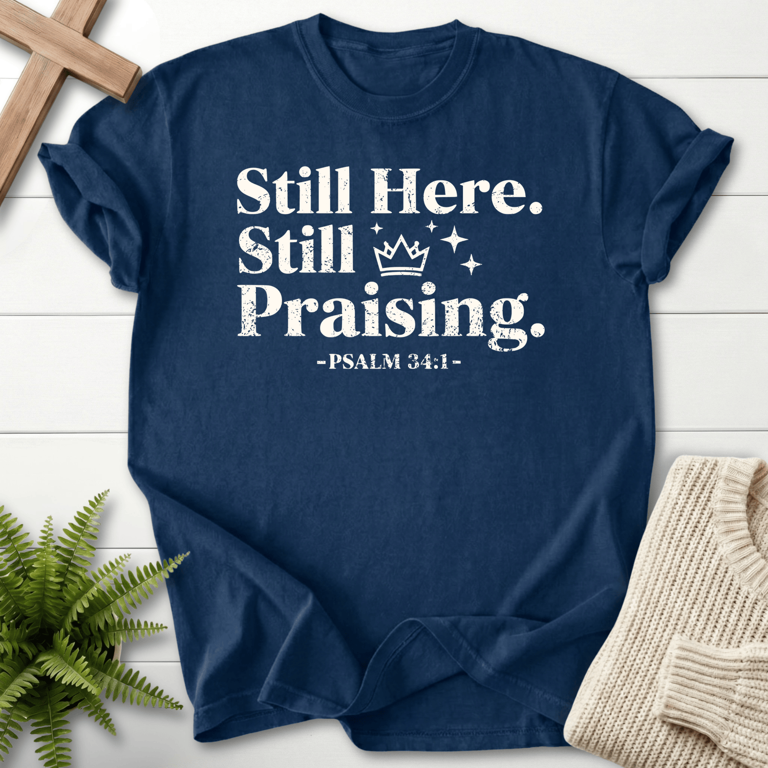 Navy Christian t-shirt for women with distressed white Still Here, Still Praising text, a crown motif, and Psalm 34:1.